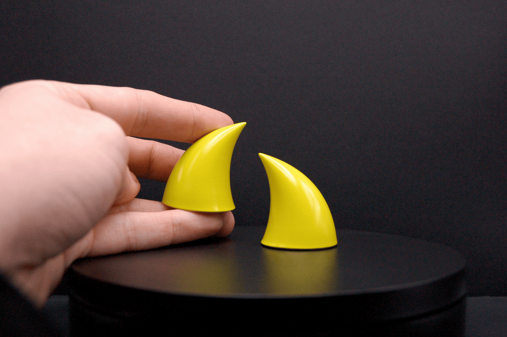 Hand holding an imp devil horn in sulfur yellow with a glossy finish.