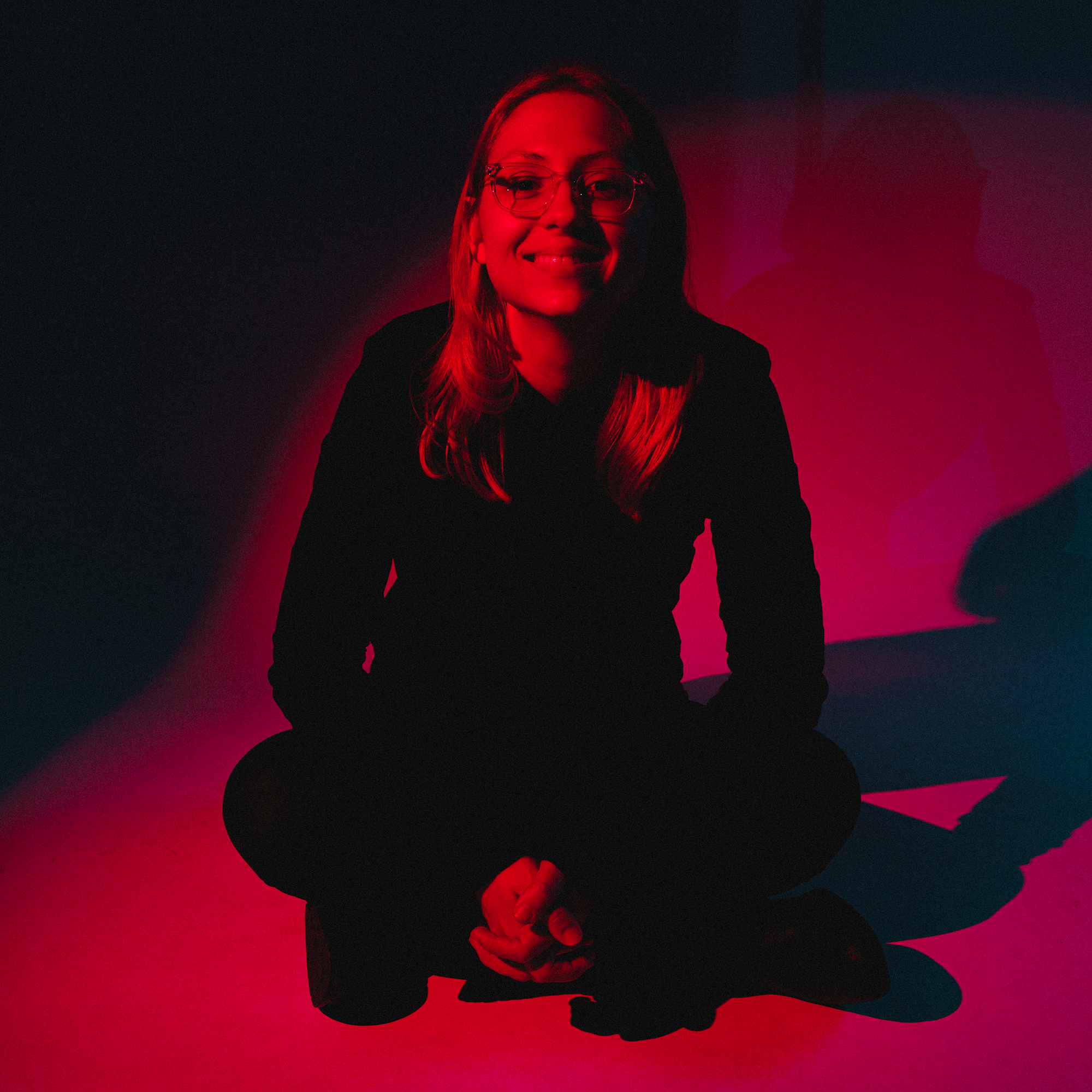 Creator Harley Brimstone sits crossed legged in red lighting.