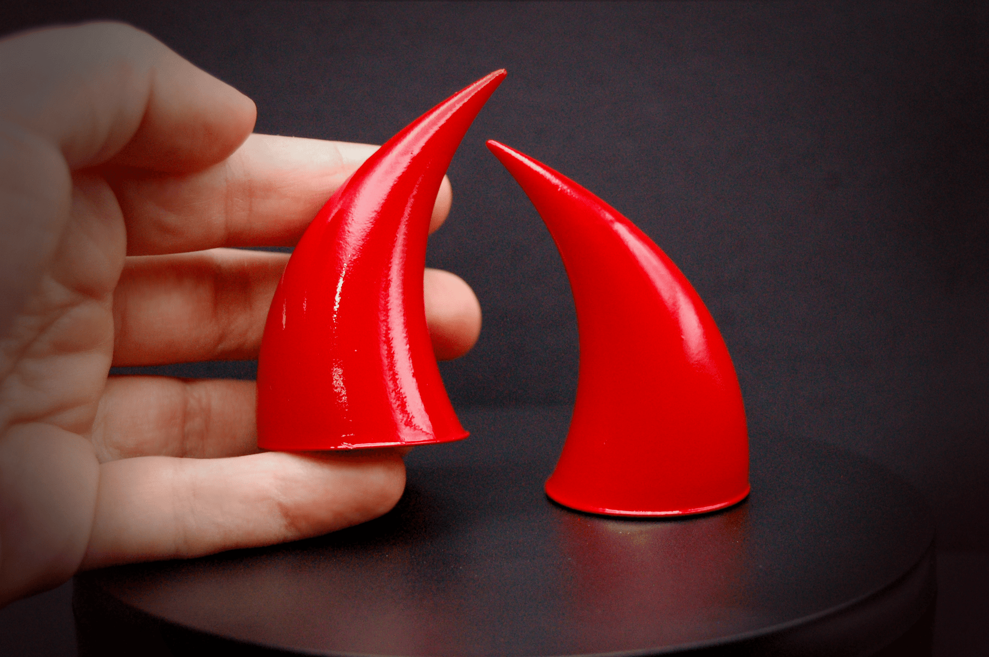 A hand holding an incubus devil horn in scarlet red with a glossy finish.