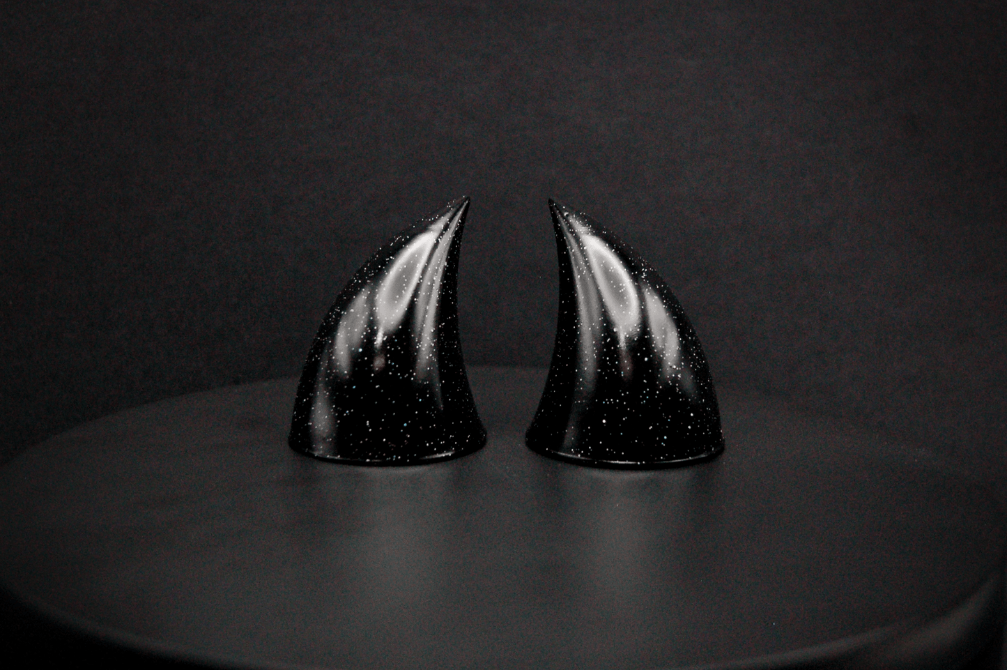 A pair of small black devil horns with a glitter finish.