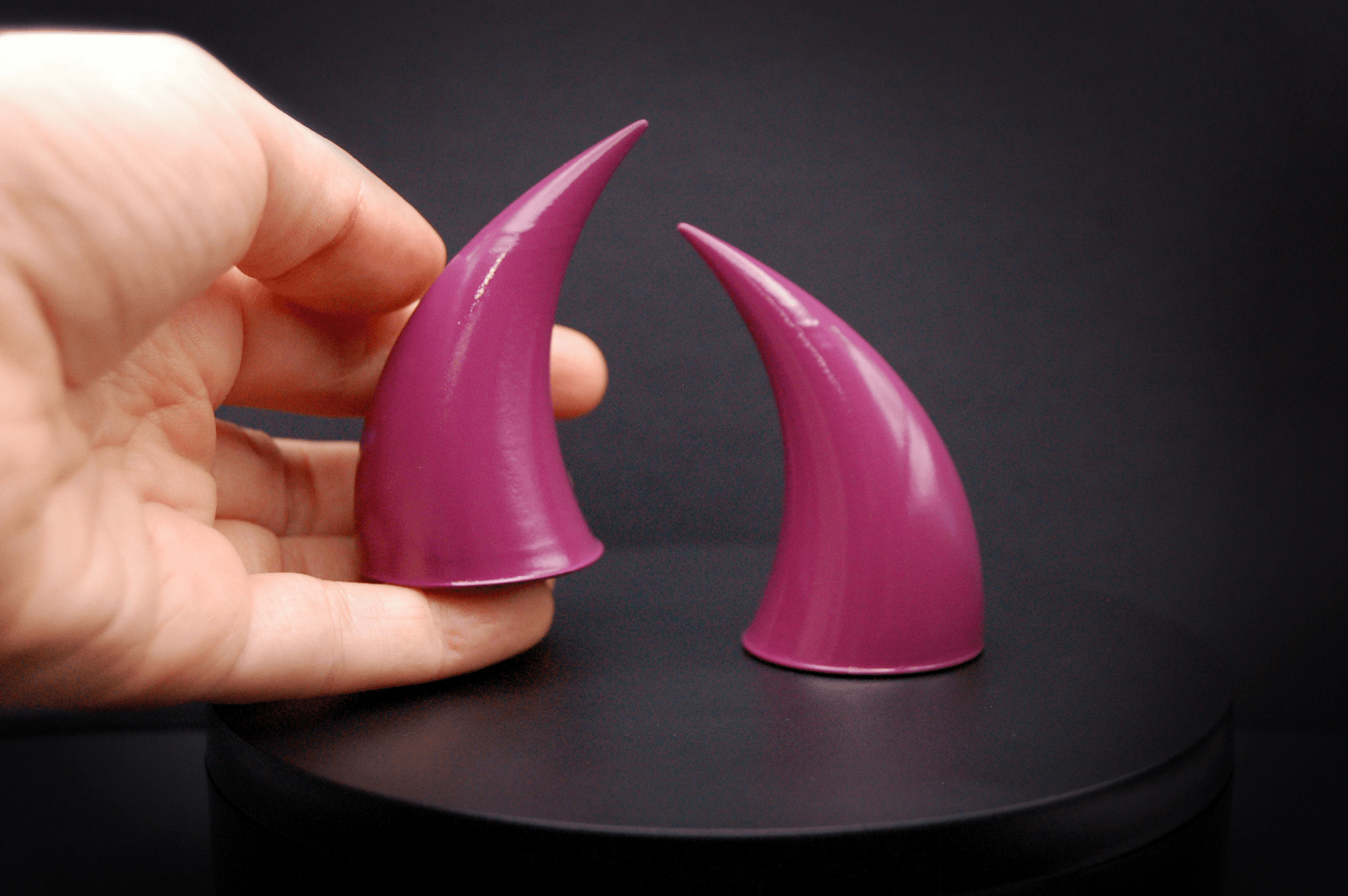 A hand holding an incubus devil horn in deep rose with a glossy finish.