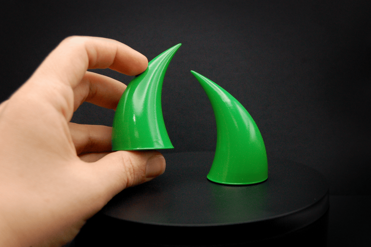 A hand holding an incubus devil horn in goblin green, a bright green with a glossy finish.