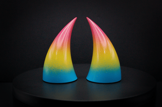 Front view of imp devil horns in a sky blue, to bright yellow, to warm pink ombré, the colors of the pansexual pride flag with a glittery finish.