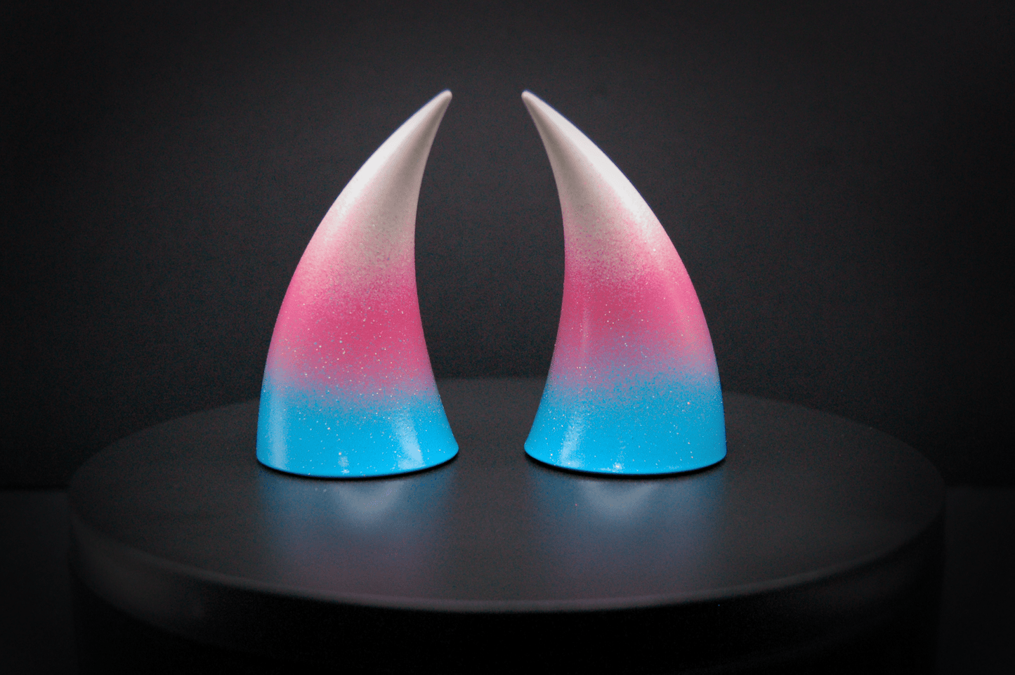 Back view of imp devil horns in a light blue, medium pink, and white ombré, the colors of the trans pride flag with a glittery finish.