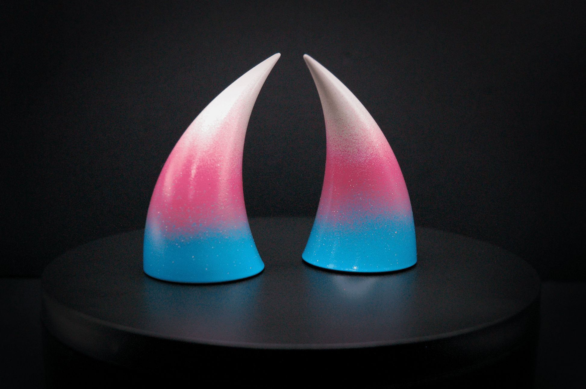 Side view of imp devil horns in a light blue, medium pink, and white ombré, the colors of the trans pride flag with a glittery finish.